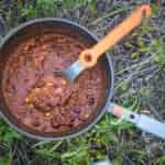 A backpacking pot filled with quinoa chili sitting on a grassy surface